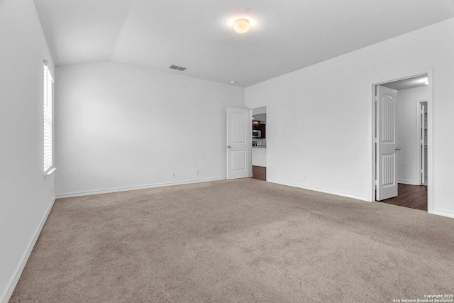 carpeted empty room featuring baseboards, vaulted ceiling, and visible vents