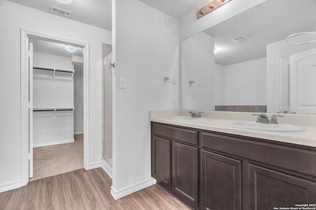 full bathroom featuring visible vents, wood finished floors, a spacious closet, a shower stall, and a sink