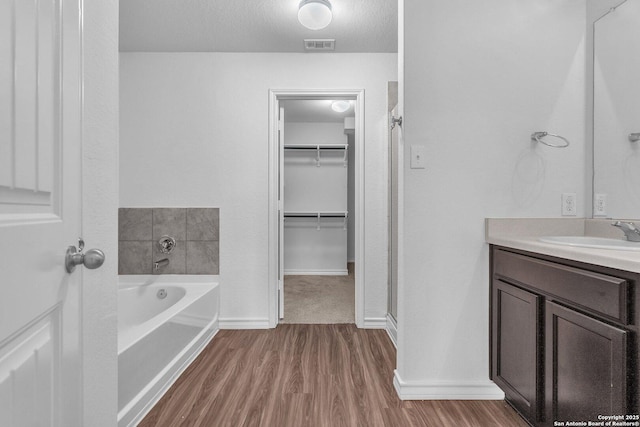 full bath with vanity, visible vents, wood finished floors, a walk in closet, and a bath