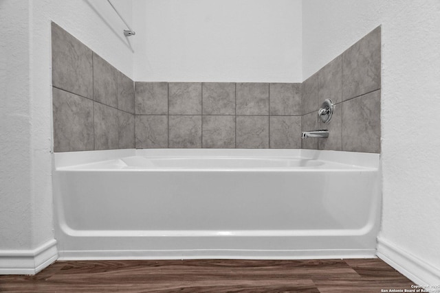 bathroom featuring wood finished floors, baseboards, a textured wall, and a bath
