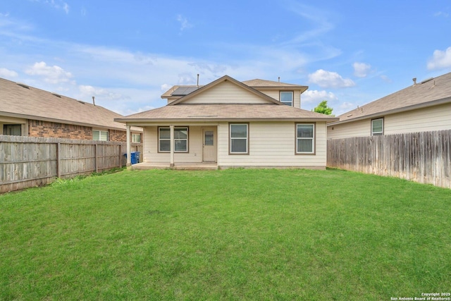 back of house with a lawn, roof mounted solar panels, and a fenced backyard