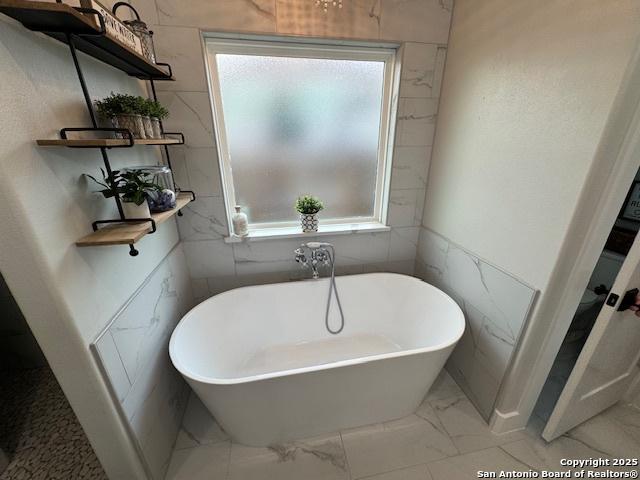 bathroom featuring a freestanding tub and marble finish floor