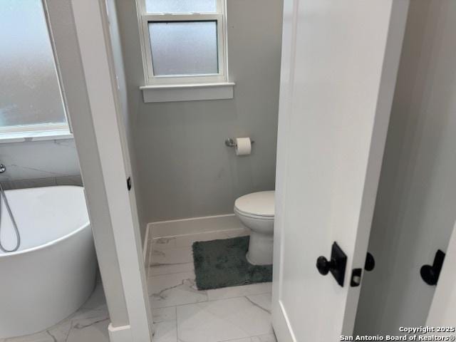 bathroom featuring baseboards, marble finish floor, a freestanding tub, and toilet
