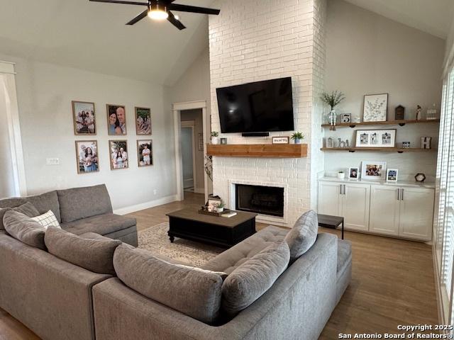 living room featuring a ceiling fan, a fireplace, wood finished floors, and high vaulted ceiling