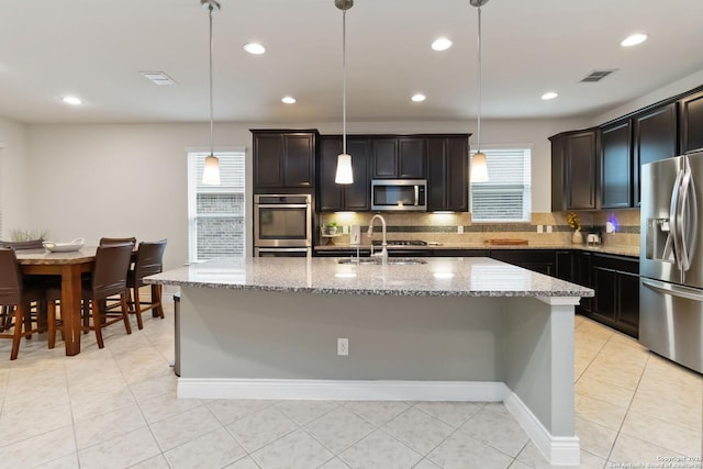kitchen featuring backsplash, visible vents, appliances with stainless steel finishes, a sink, and light stone counters
