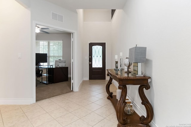 foyer with ceiling fan, light colored carpet, visible vents, baseboards, and light tile patterned flooring