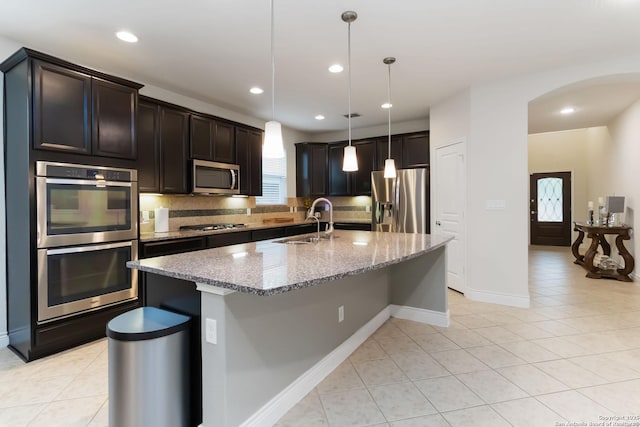 kitchen with light tile patterned floors, light stone countertops, stainless steel appliances, and a sink