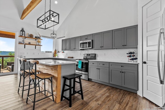 kitchen featuring a breakfast bar, high vaulted ceiling, gray cabinets, stainless steel appliances, and decorative backsplash