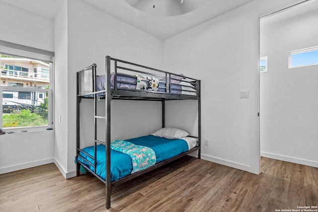 bedroom with baseboards, wood finished floors, and multiple windows