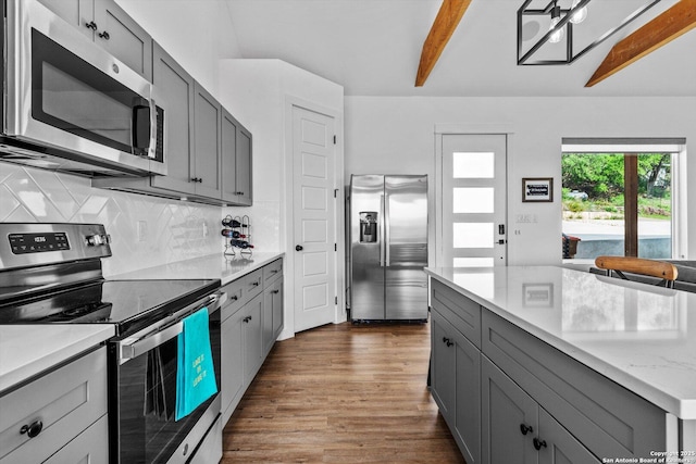 kitchen featuring beam ceiling, gray cabinets, dark wood finished floors, backsplash, and stainless steel appliances