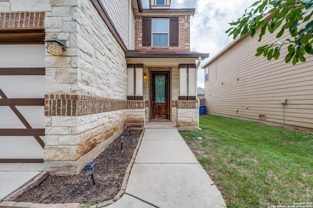 view of exterior entry featuring a lawn, brick siding, and stone siding