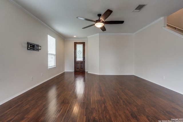 empty room featuring ceiling fan, ornamental molding, baseboards, visible vents, and dark wood-style floors