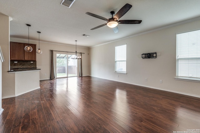 unfurnished living room featuring dark wood-style flooring, visible vents, baseboards, ceiling fan with notable chandelier, and ornamental molding