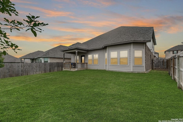 back of property featuring a lawn, a shingled roof, and a fenced backyard