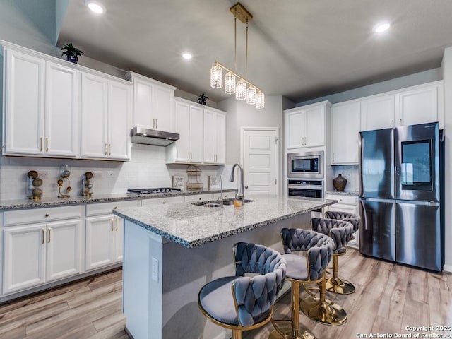 kitchen featuring a kitchen bar, white cabinetry, a sink, backsplash, and stainless steel appliances