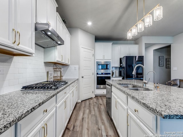 kitchen with wall chimney exhaust hood, white cabinets, a sink, light wood-style flooring, and stainless steel appliances