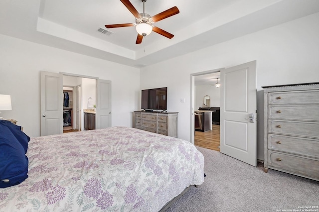 bedroom with ceiling fan, visible vents, a raised ceiling, connected bathroom, and carpet flooring