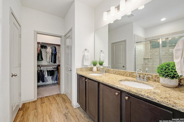 full bath with a sink, double vanity, a shower stall, and wood finished floors