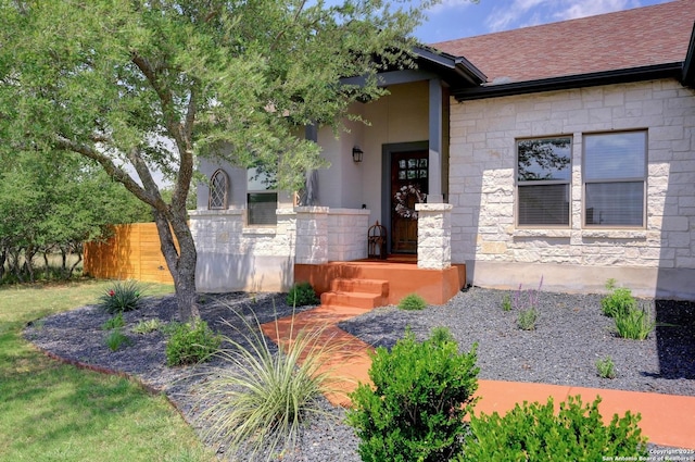 view of exterior entry featuring roof with shingles, fence, and stone siding