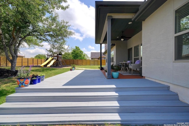 deck with a yard, a ceiling fan, a fenced backyard, and a playground