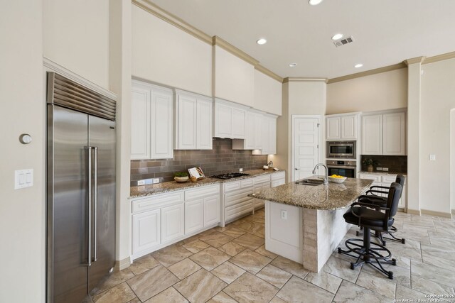 kitchen with visible vents, decorative backsplash, built in appliances, white cabinetry, and a sink