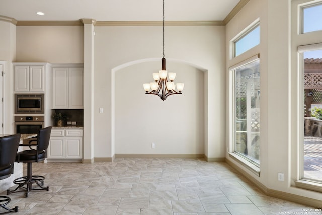 unfurnished dining area featuring crown molding, baseboards, a high ceiling, and a notable chandelier