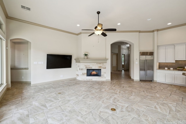 unfurnished living room with crown molding, arched walkways, a ceiling fan, baseboards, and visible vents