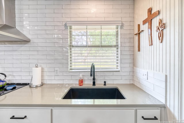 kitchen with light countertops, a sink, wall chimney exhaust hood, and tasteful backsplash