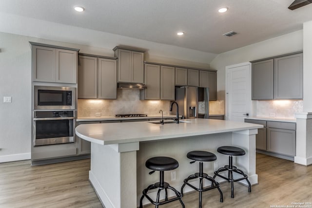 kitchen featuring a sink, gray cabinets, a center island with sink, and stainless steel appliances