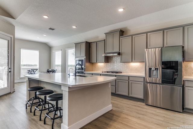kitchen with light wood-style floors, gray cabinets, a kitchen island with sink, a sink, and stainless steel fridge