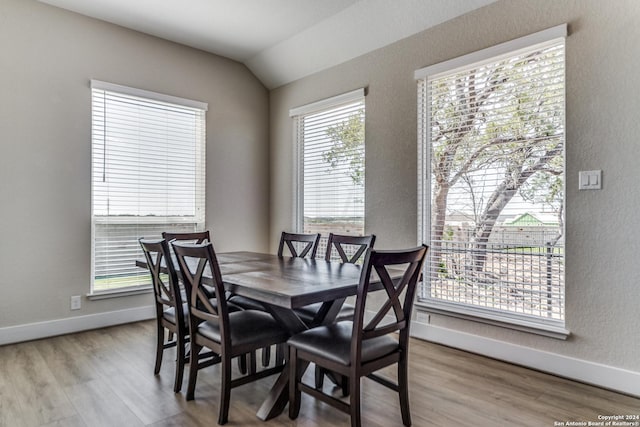 dining room featuring baseboards, a textured wall, wood finished floors, and vaulted ceiling