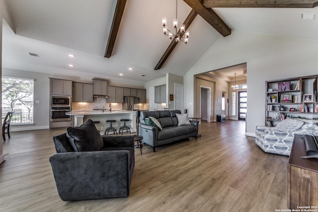 living area featuring an inviting chandelier, beam ceiling, baseboards, high vaulted ceiling, and light wood finished floors