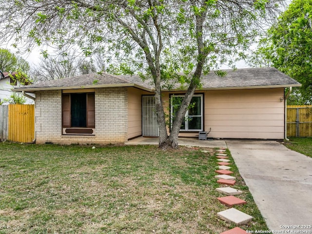 ranch-style house with brick siding, fence, roof with shingles, and a front lawn