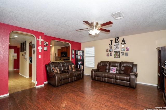 living room with arched walkways, a textured ceiling, a ceiling fan, wood finished floors, and visible vents