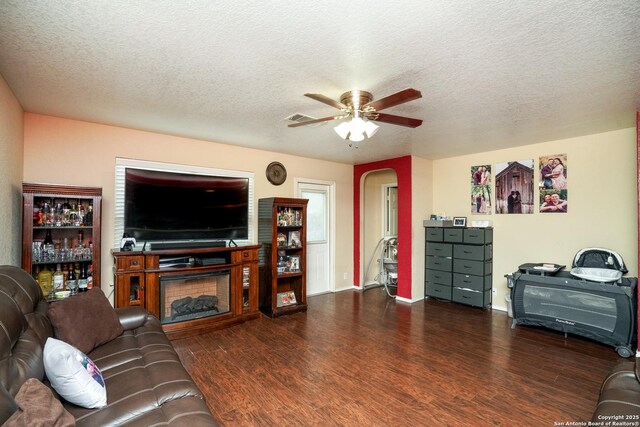 living area with ceiling fan, dark wood-style flooring, a textured ceiling, visible vents, and arched walkways