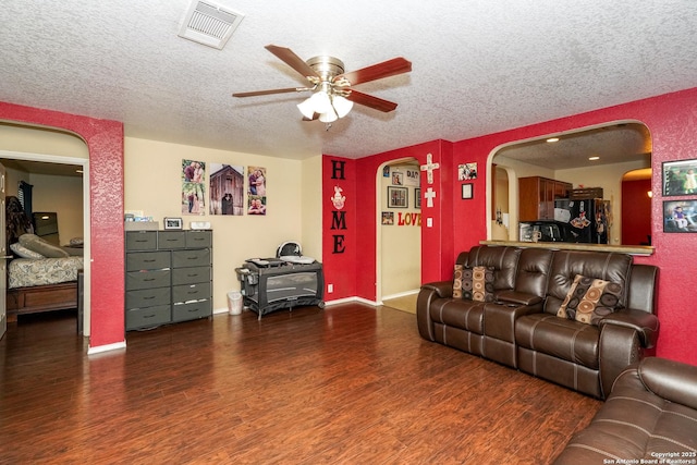 living room with arched walkways, a textured ceiling, a ceiling fan, wood finished floors, and visible vents