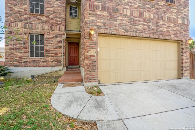doorway to property with a garage, driveway, and brick siding