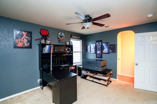 carpeted office with visible vents, a ceiling fan, baseboards, a textured ceiling, and arched walkways