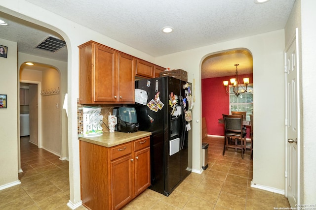 kitchen with arched walkways, an inviting chandelier, black fridge, and light tile patterned floors