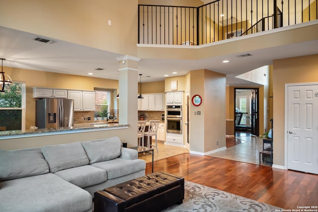 living room featuring visible vents, a towering ceiling, plenty of natural light, and wood finished floors