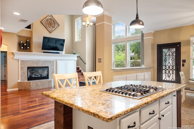 kitchen featuring light stone countertops, white cabinetry, open floor plan, stainless steel gas stovetop, and pendant lighting