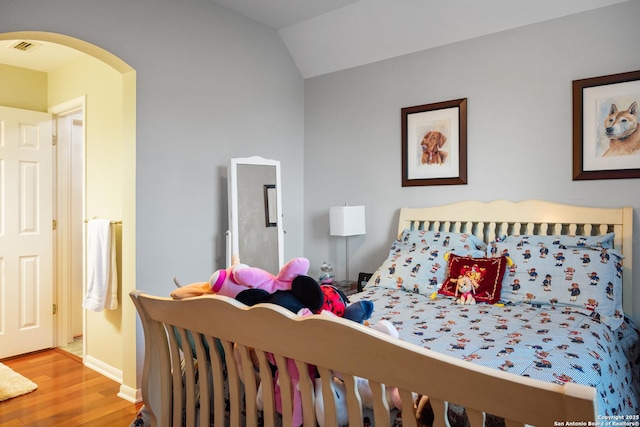 bedroom with visible vents, arched walkways, vaulted ceiling, wood finished floors, and baseboards