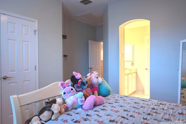 bedroom featuring visible vents, attic access, arched walkways, and ensuite bath
