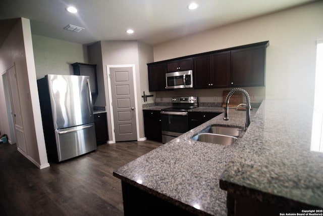kitchen with light stone countertops, dark wood finished floors, a sink, stainless steel appliances, and recessed lighting