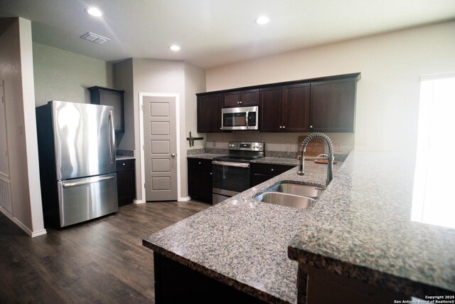 kitchen featuring dark brown cabinets, a sink, a peninsula, stainless steel appliances, and dark wood-type flooring