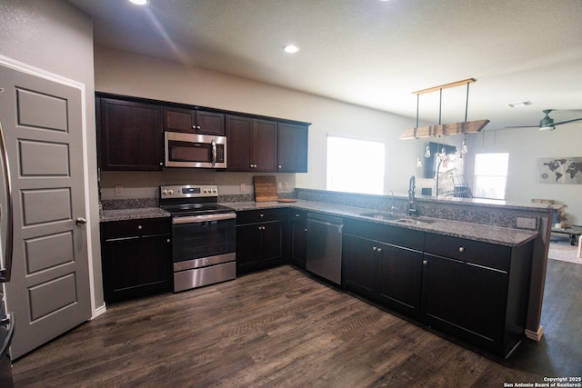 kitchen with stainless steel appliances, dark wood-style floors, a sink, and a peninsula