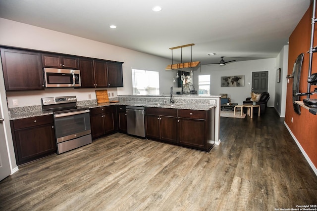 kitchen with a peninsula, dark brown cabinetry, ceiling fan, dark wood finished floors, and appliances with stainless steel finishes