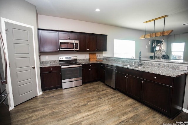 kitchen featuring light stone counters, a sink, stainless steel appliances, a peninsula, and dark wood-style floors