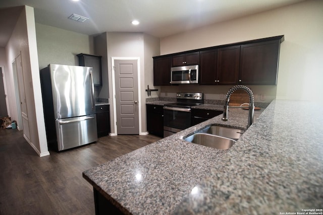 kitchen with dark brown cabinets, appliances with stainless steel finishes, a sink, visible vents, and dark wood-style floors
