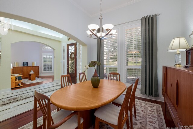 dining room featuring a notable chandelier, arched walkways, baseboards, wood finished floors, and ornamental molding